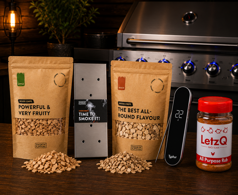 Ultimate Fish Gas Experience Bundle met Typhur InstaProbe Core, LetzQ All Purpose Rub, Smokin' Flavours appel- en beukenrooksnippers en RVS smokerbox op een houten tafel met gasbarbecue op de achtergrond.